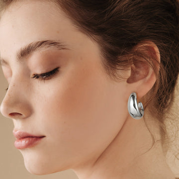 Golden/Silvery-colored, C-shaped earrings with two pointed tips and a wide middle